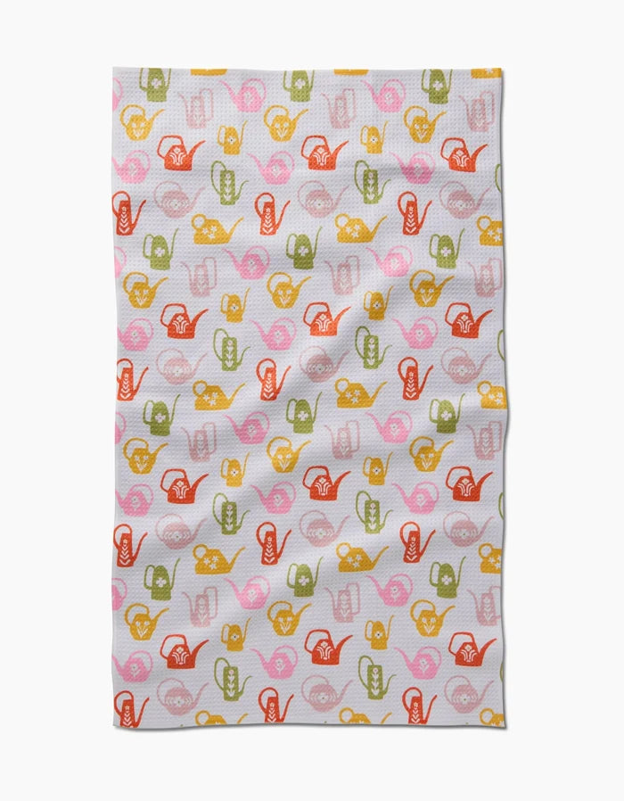 The Kayla Ann Retro Watering Cans Tea Towel features colorful illustrations of watering cans and garden tools in red, pink, yellow, and green on white—crafted from recycled materials for eco-friendly appeal.