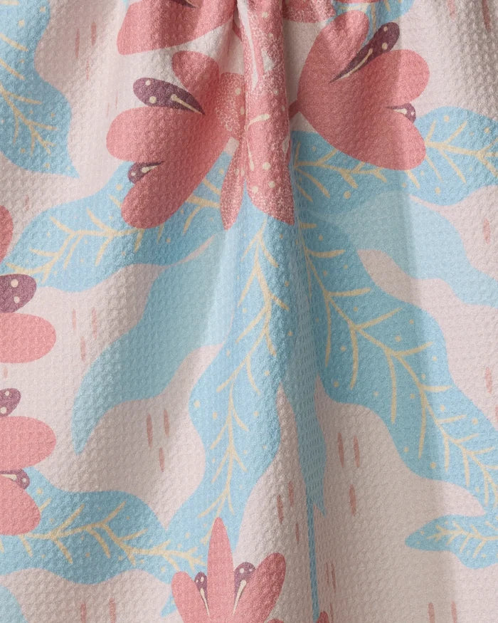 Close-up of the Julianne Haness Rhododendron quick-drying tea towel made from recycled materials, featuring textured fabric with large pink flowers, blue leaves, and yellow accents on a light background.