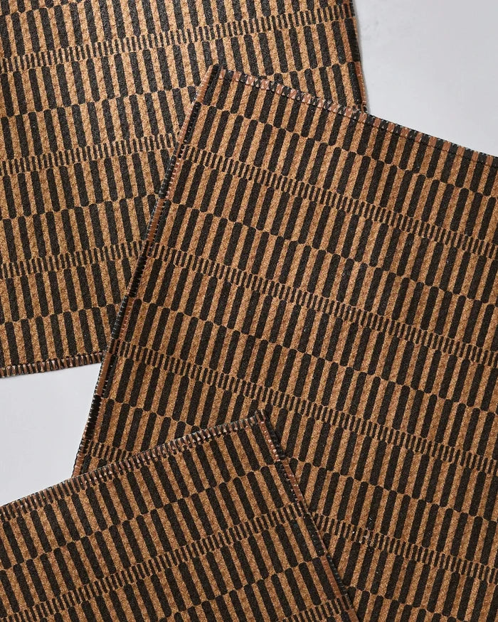 Four Ridge cork placemats by Geometry, featuring a repeating black geometric vertical line pattern, arranged overlapping on a white surface. Made from recycled materials for an eco-friendly touch.
