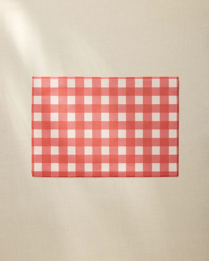 A Ripe Tomato Gingham placemat by Geometry, featuring a red and white checkered design, rests on a plain beige surface.