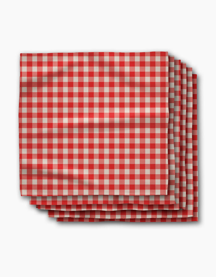 Four folded Ripe Tomato Gingham napkins by Geometry, featuring a red and white checkered pattern, are stacked neatly on a white background. Made from Geosuede fabric, this set blends softness with sustainable style.