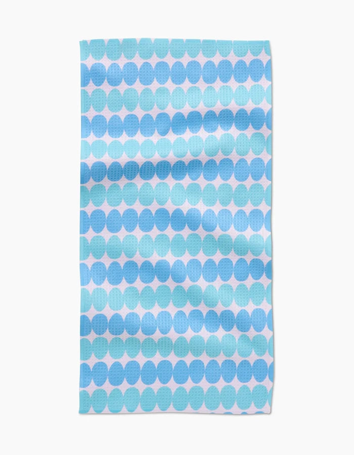 The Kayla Ann Robins Egg Bar Towel features a blue and light blue circle pattern on white Geoweave fabric. With visible folds and a slightly textured surface, it combines style with durability.