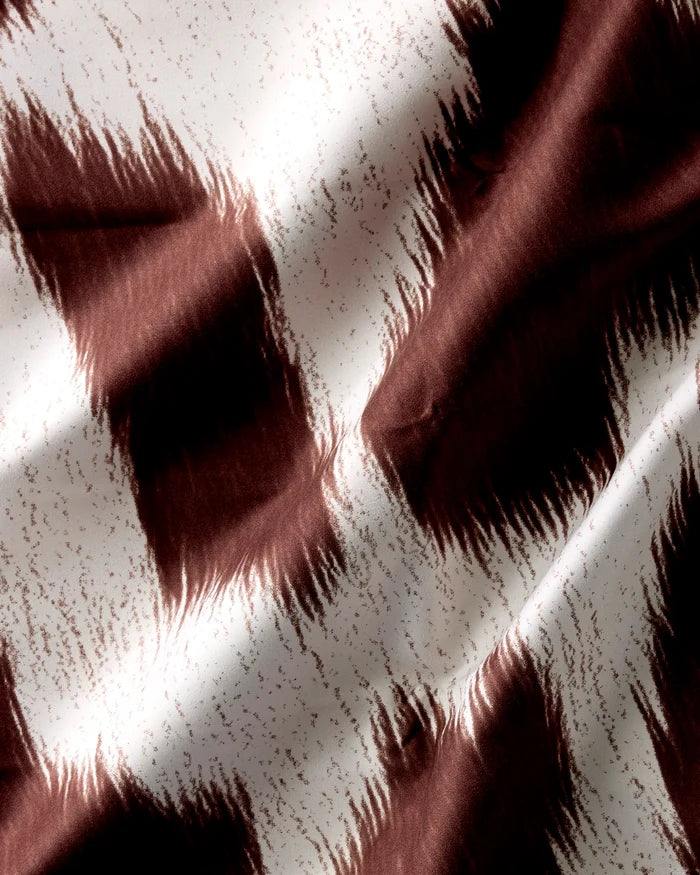 A close-up of Geometry's Rodeo reusable cloth napkins shows abstract, jagged brown and white brushstroke patterns. The soft fabric folds create dynamic shadows and highlights.