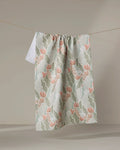 The Amy MacCready Rollie, a recycled kitchen towel with green leaves and peach flowers, hangs from a clothesline against a neutral background.