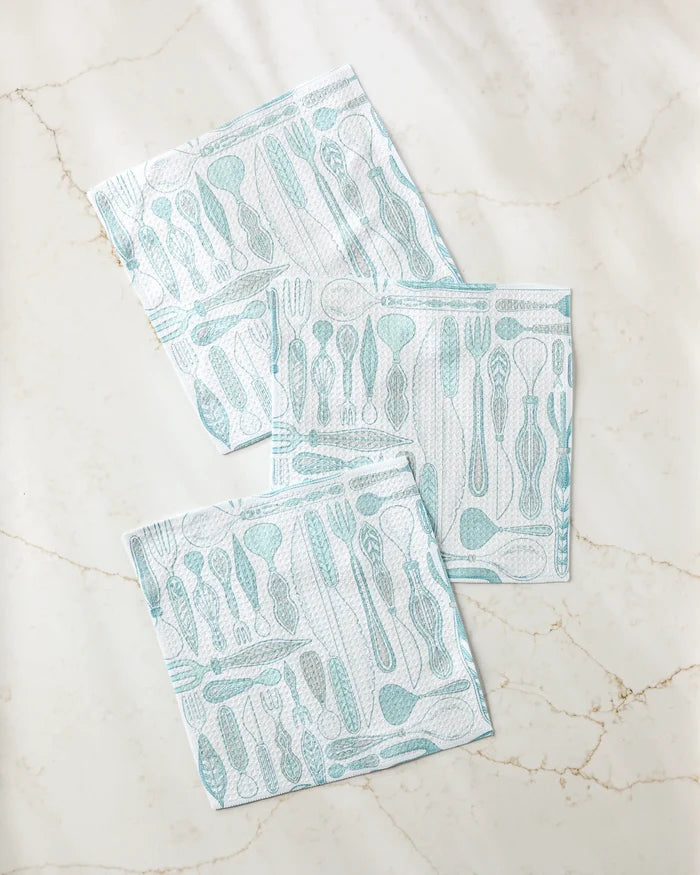 Three Romy Wares blue and white super-absorbent dishtowels by Amy MacCready, featuring various utensil patterns, are arranged with slight overlap on a light marble-like surface.