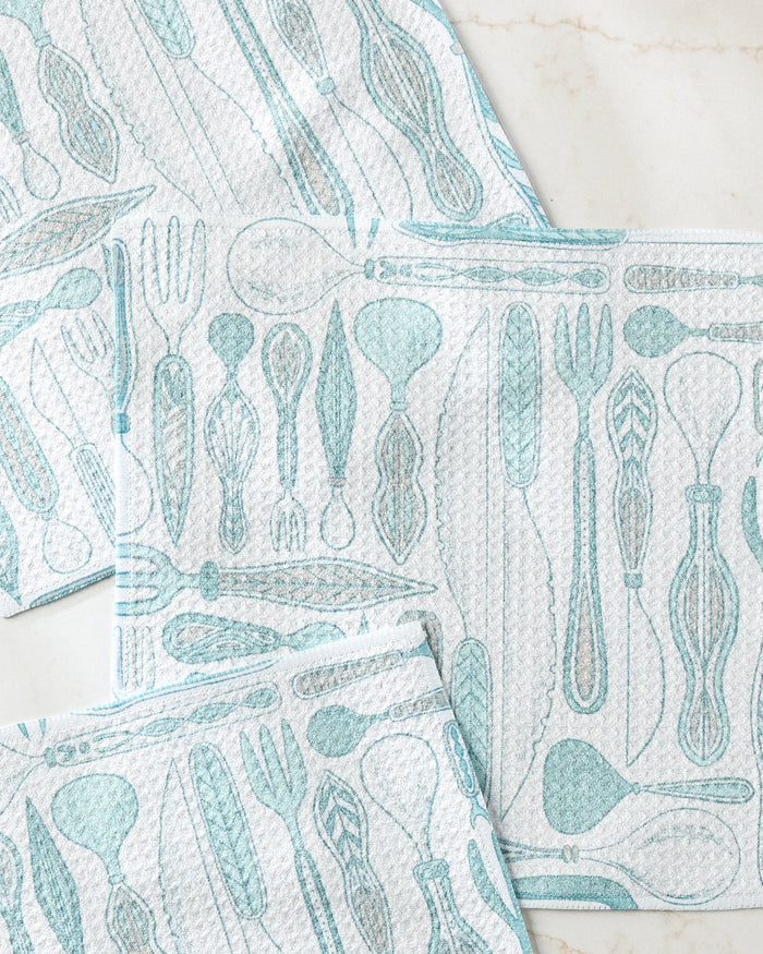 Three white Romy Wares dishcloths by Amy MacCready, featuring a light blue cutlery pattern, are arranged on marble—an eco-friendly recycled set perfect for any kitchen.
