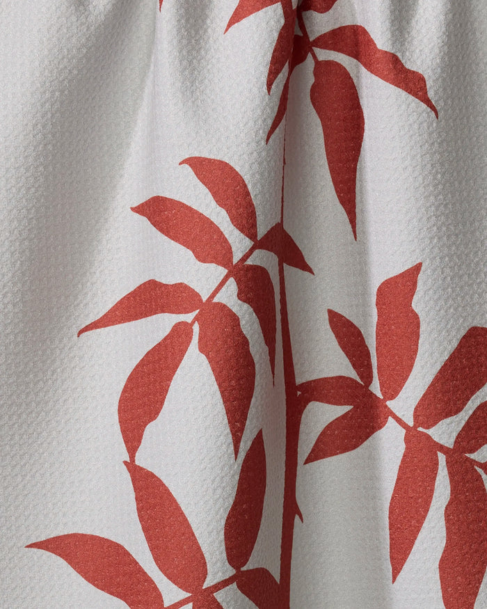 Close-up of PrintedPlant's "Rose" kitchen towel in white textured fabric, showcasing a bold red leafy branch pattern. The stylized leaves spread across the absorbent towel, with soft folds enhancing its eco-friendly design and depth.