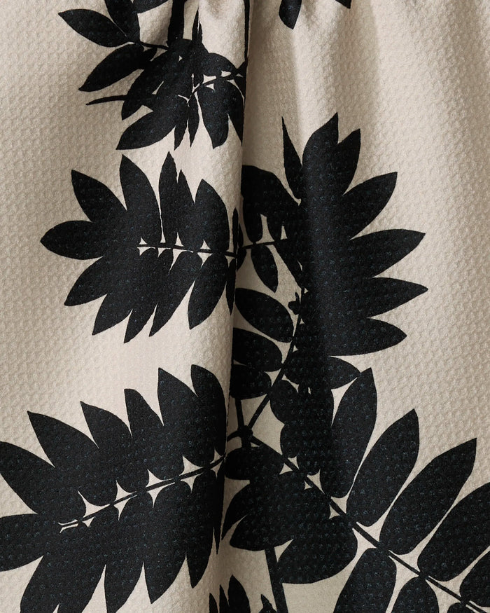 The Rowan kitchen towel by PrintedPlant features ultra-absorbent, recycled beige fabric with a bold black leafy plant design. Large overlapping leaves create a striking contrast against the textured light background.
