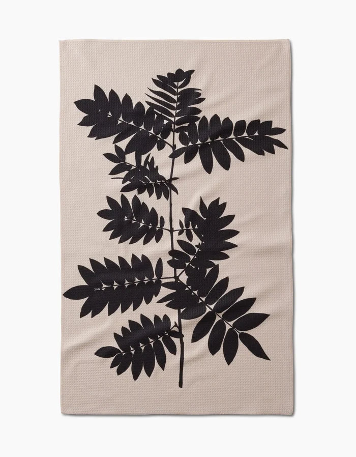 The Rowan tea towel by PrintedPlant features a bold black leafy branch silhouette on beige ultra-absorbent Geoweave fabric with a plain background and organic leaf shapes.