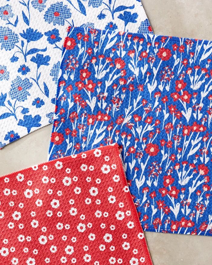 The Danelys Sidron "Royal Garden" set features three square dishcloths made from recycled materials, each with floral patterns: red with white flowers, blue with red and white, and white with blue and red.