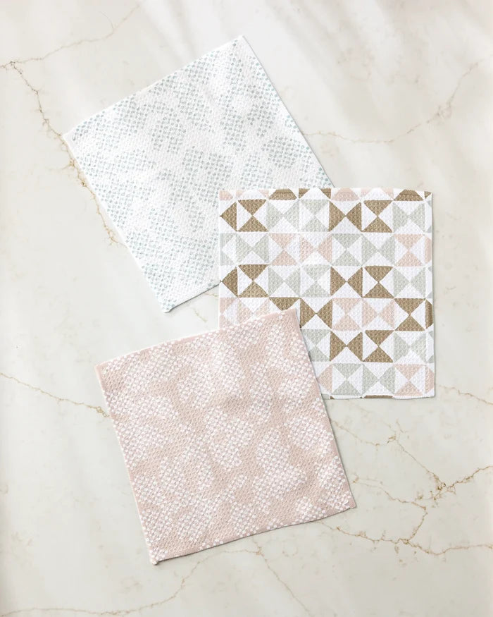 Studio Jeannot's Rubix Pixie set includes three square recycled dishcloths: two with pink and light blue dotted patterns, and one with pink, beige, and gray triangles—sustainable style for your kitchen.