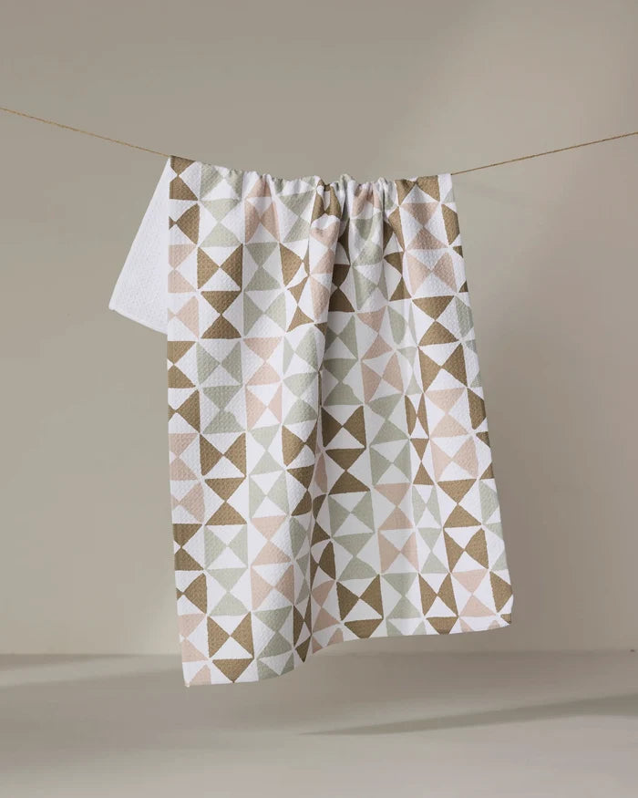 The Rubix tea towel by Studio Jeannot, featuring a geometric pattern in beige, brown, and white, hangs on a clothesline against a neutral background.