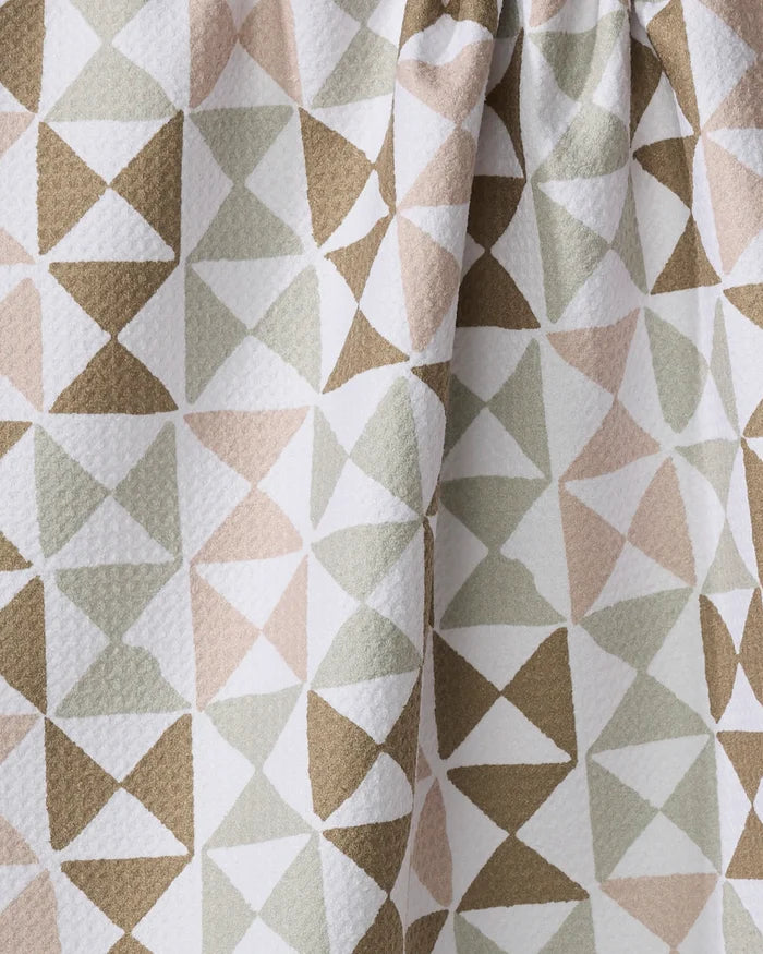 Close-up of the Rubix tea towel by Studio Jeannot, featuring a geometric pattern of overlapping triangles in beige, taupe, olive green, and white. The textured fabric is slightly gathered at the top.