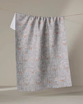 The Rulon Grey kitchen towel by Becki Owens, featuring a textured gray finish with white and rust geometric patterns, hangs neatly over a clothesline against a softly lit neutral background.
