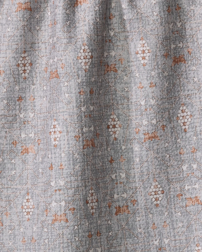 The Rulon Grey kitchen towel by Becki Owens features a geometric and floral pattern in white and brownish-orange on gray recycled fabric, with symmetrical diamond and leaf shapes. Its slightly wrinkled texture adds soft folds and subtle shadows.