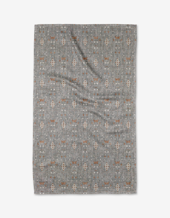 The Becki Owens Rulon Grey area rug features a subtle patterned design in muted gray, brown, and beige tones on Geoweave fabric. Displayed on a white background, there is a slight wrinkle visible in the center.