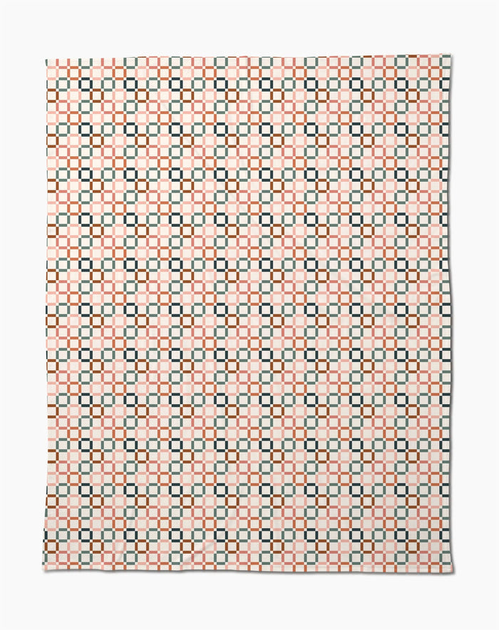 The Russet Crossroads Butter Blanket by Charlie Rowan Designs features a symmetrical geometric pattern of black squares and orange lines on white, crafted from recycled materials for an eco-friendly, stylish look.
