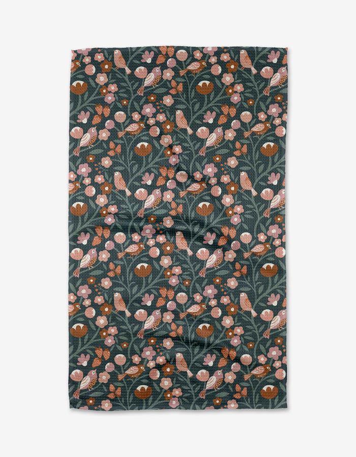 The Charlie Rowan Designs Russet Park Lane Tea Towel features a dark green background with a lively botanical pattern of orange and pink birds, pink flowers, and green leaves. Made from eco-friendly Geoweave™ fabric with recycled materials.