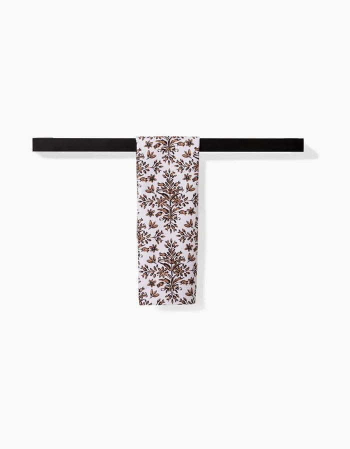The Hufton Studio Rustic Lacy Tile Natural towel, featuring a brown floral design on white, hangs neatly over a sleek black rod against a plain white background.