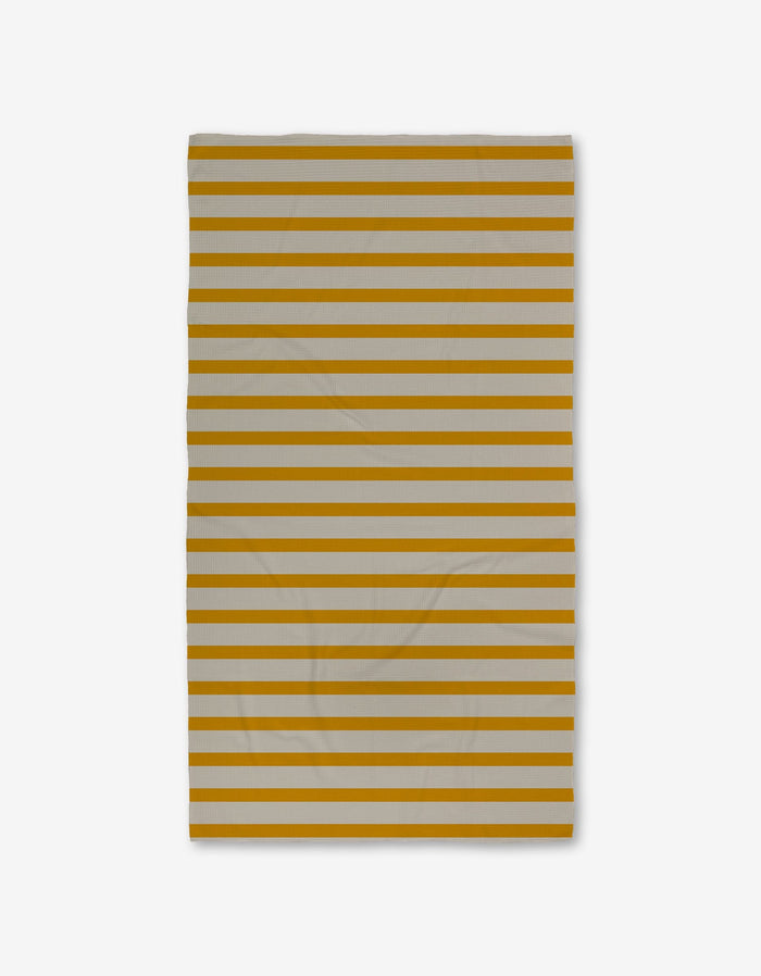 The GEOMETRY Saffron Stripes Luxe Bath Towel, with alternating horizontal mustard yellow and light gray stripes, is shown against a white background. The Geoweave fabric has slight wrinkles.