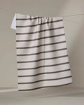 The Jenny Keller Salt Air Stripe tea towel, featuring quick-drying white fabric with evenly spaced horizontal black stripes, hangs on a clothesline against a neutral background.