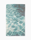 The Geometry Saltwater Glow Tea Towel features a print of sunlight on clear blue water, evoking a swimming pool, and is made from absorbent Geoweave fabric.