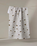 The "San Diego" tea towel by Amy MacCready features white absorbent fabric with light gray fan patterns and small brown dot clusters, shown hanging from a string against a neutral background.