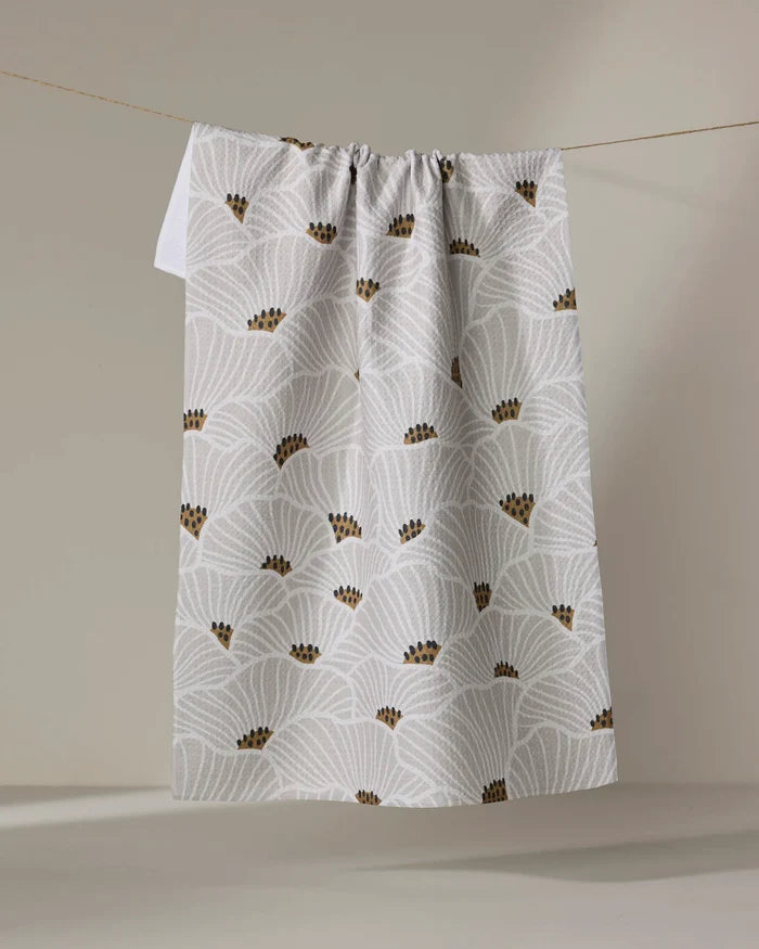 The "San Diego" tea towel by Amy MacCready features white absorbent fabric with light gray fan patterns and small brown dot clusters, shown hanging from a string against a neutral background.