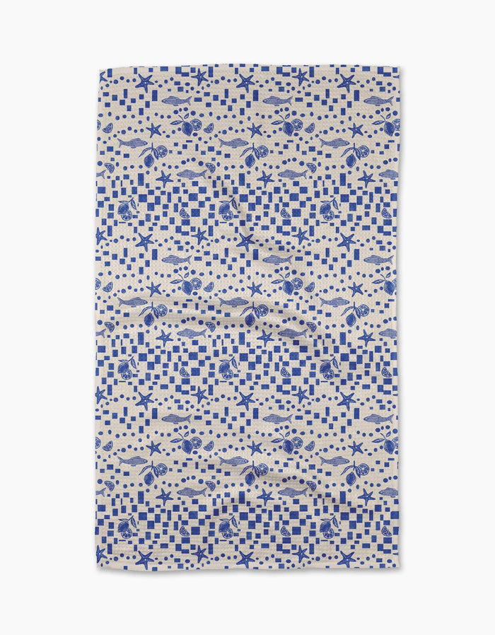 The Santorini Tile Tea Towel by Geometry is a rectangular beige towel with a blue nautical pattern of fish, seashells, starfish, and checkerboard designs. Made from recycled materials, it’s shown flat on a white background.