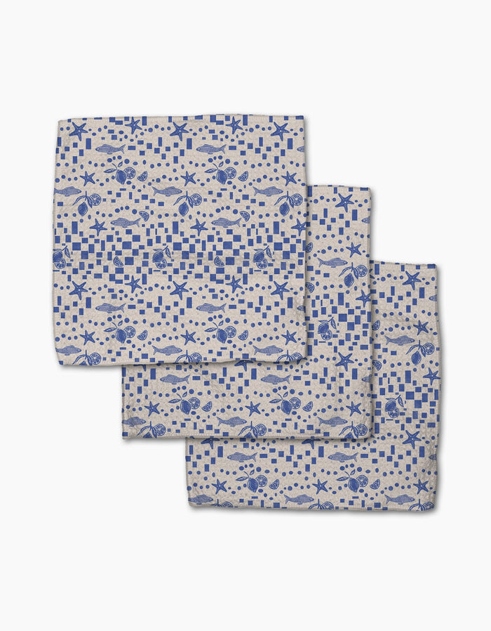 Three folded Geometry Santorini Tile dishcloths, featuring blue nautical patterns of fish, crabs, seashells, and checkered squares on beige Geoweave fabric, are arranged overlapping on a white background.