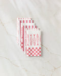 Five folded Sardine Check Red reusable paper towels by Hufton Studio, featuring red fish and checkerboard patterns, are arranged in a fan shape on a white marble surface.