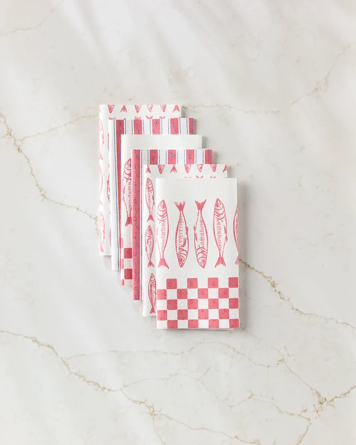 Five folded Sardine Check Red reusable paper towels by Hufton Studio, featuring red fish and checkerboard patterns, are arranged in a fan shape on a white marble surface.