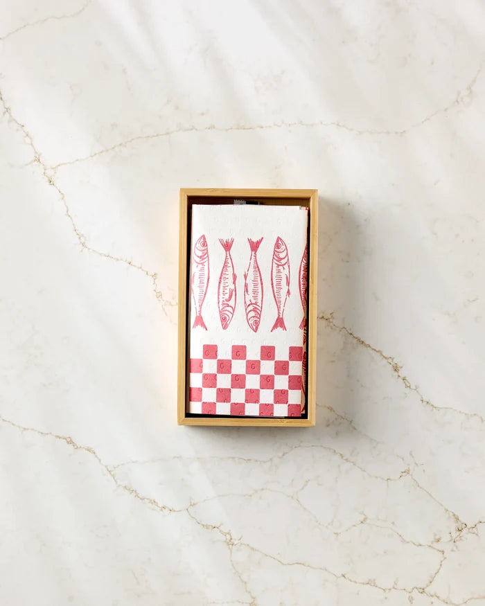 A box displays Hufton Studio's Sardine Check Red: a white notepad with four red fish illustrations and a checkerboard pattern, set on light marble—ideal for notes or pairing with eco-friendly paper towels.