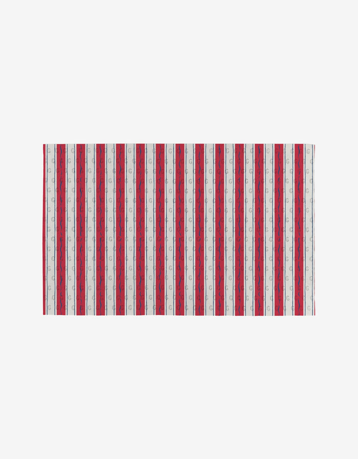 The Sardine Check Red towel by Hufton Studio features vertical red, white, and blue stripes—some with a repeating small logo—on a plain white background. Made from post-consumer recycled materials, it’s an eco-friendly choice.