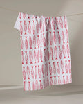 The "Sardine Stripes" tea towel by Hufton Studio features a repeating red fish pattern and is shown hanging on a clothesline against a neutral background.