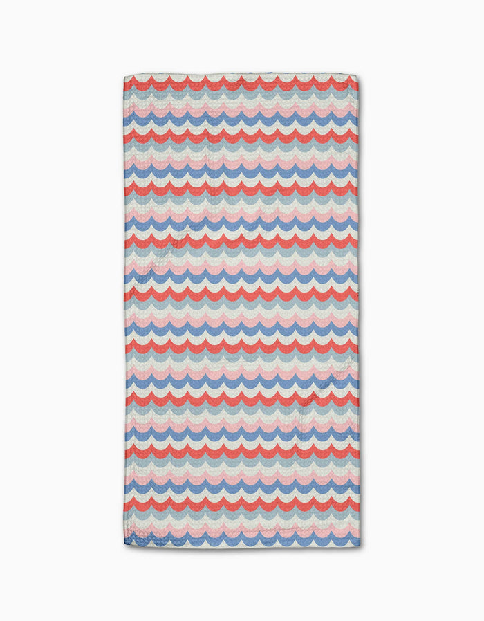 The Geometry Scallop Stripes Bar Towel features a blue, red, and white scalloped wave pattern on cream. Made from durable Geoweave fabric for superior absorbency and quick drying, shown flat on a white surface.