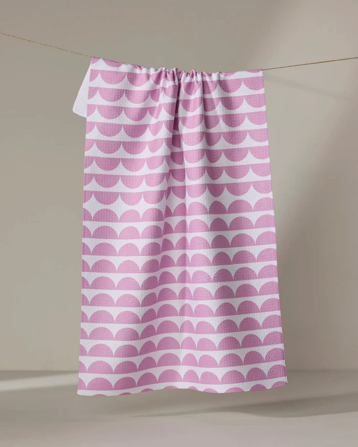 The Buy Guide's "Scallops - Pink" eco-friendly dish towel features a pink and white repeating scallop pattern, shown hanging against a neutral background.
