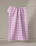 The Buy Guide's "Scallops - Pink" eco-friendly dish towel features a pink and white repeating scallop pattern, shown hanging against a neutral background.