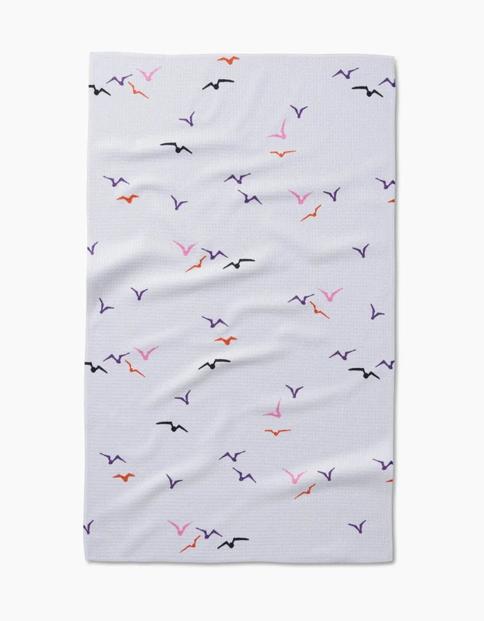 The Scattered Seagulls blanket by Ania Zwara Art is a white, textured throw made from recycled materials, featuring simple black, purple, orange, and pink seagull motifs scattered across the surface.