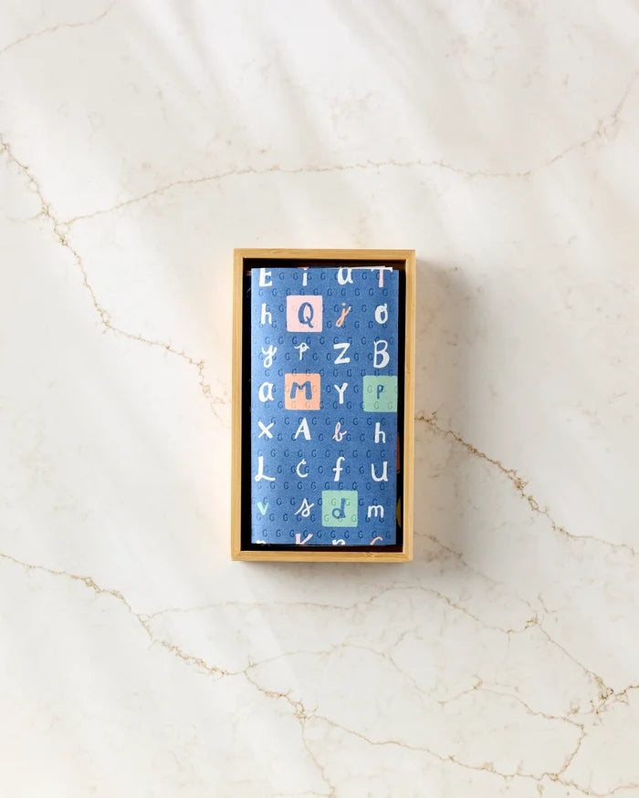 A rectangular "School Days" box by Amy MacCready, made from post-consumer recycled materials, has a blue lid with colorful alphabet letters in various sizes. The box sits on a light marble surface and is viewed from above.