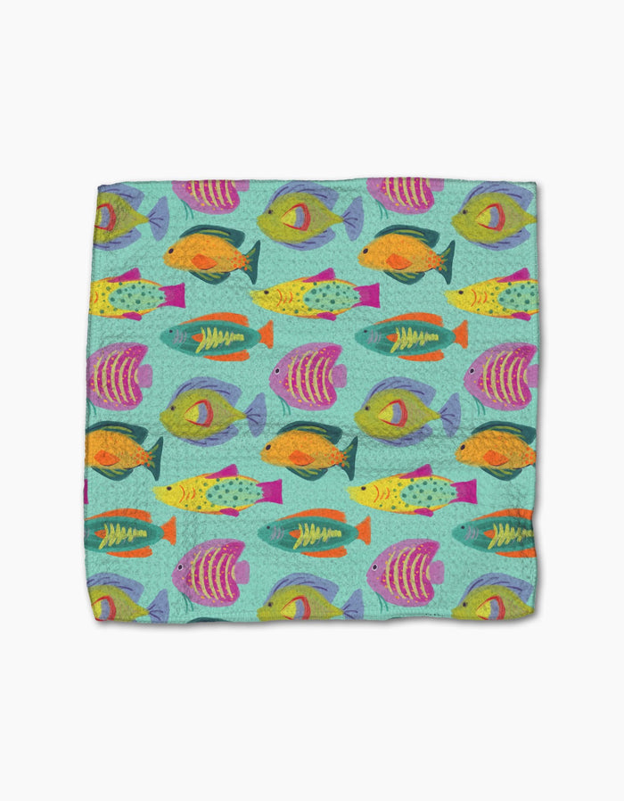 The Geometry Schooling towel is a rectangular, super-absorbent piece featuring a vibrant pattern of tropical fish in orange, yellow, green, purple, and blue on light blue. Made from post-consumer recycled materials for eco-friendliness.