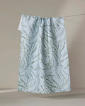 Katie O'Shea's Sea Forest recycled kitchen towel, in pale blue with a subtle green botanical pattern, hangs on a thin clothesline against a neutral beige background.