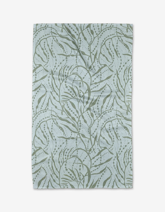 The Sea Forest Tea Towel by Katie OShea is a rectangular, light blue towel with an abstract green botanical pattern on ultra-absorbent Geoweave fabric. The slightly textured cloth displays visible folds and creases.