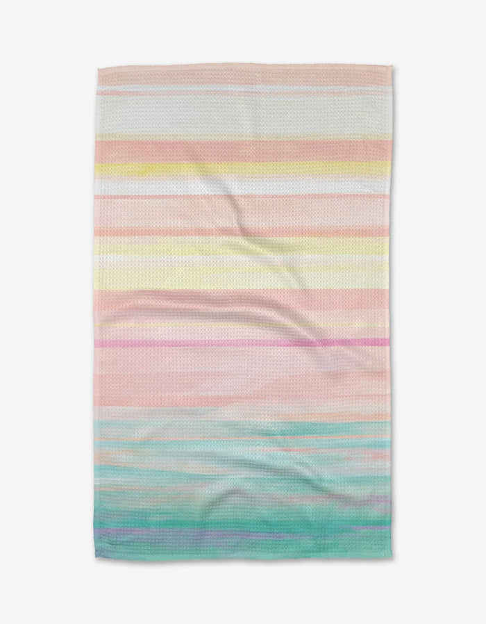 The Stefanie Bales Seafoam tea towel features textured Geoweave fabric with horizontal pastel stripes in pink, yellow, peach, lavender, blue, and green, shown laid flat on a white background.