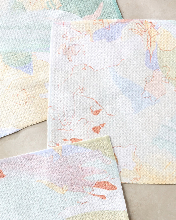 The Secret Fort dishcloth set by Kristina Baker features three super-absorbent cloths with blue, pink, yellow, and orange abstract patterns on soft, textured fabric made from recycled materials.