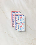 Four folded Mindfulnice Seeing Stars reusable paper towels are stacked on a light marble surface, featuring red, white, and blue star and stripe patterns for a patriotic Americana look. These eco-friendly napkins are perfect for your kitchen.
