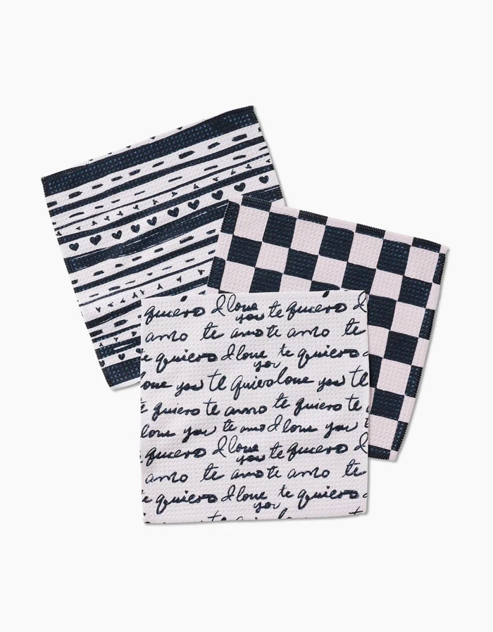 Three folded Self Love cloth napkins by Danelys Sidron, made from recycled materials and featuring black and white patterns—stripes and dots, handwritten script, and checkerboard—are arranged overlapping on a white background.