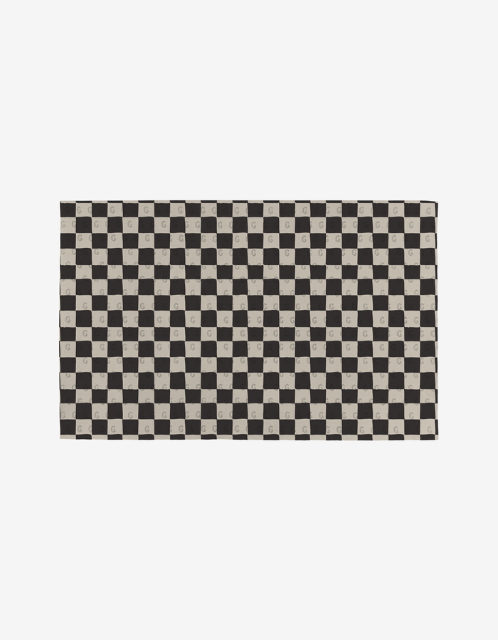 The Self Love mat by Danelys Sidron features a black and beige checkerboard pattern on eco-friendly recycled materials, with select beige squares displaying a centered G. The background is plain white.