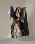 The Skye Walker Sepia Shift tea towel, featuring a geometric pattern in black, beige, and brown and made from recycled materials, hangs on a clothesline with part of a smaller white towel peeking out behind it.