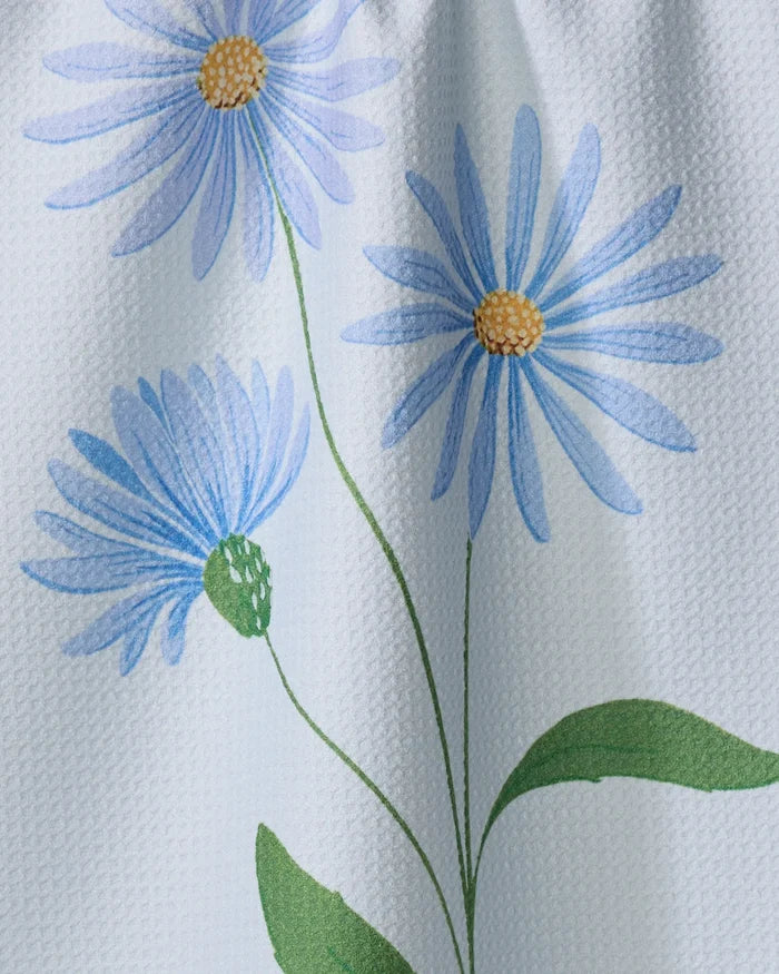 September Aster by Linda Fox features three light blue daisy-like flowers with yellow centers and green stems on a textured white background, ideal for a kitchen tea towel made from recycled materials.